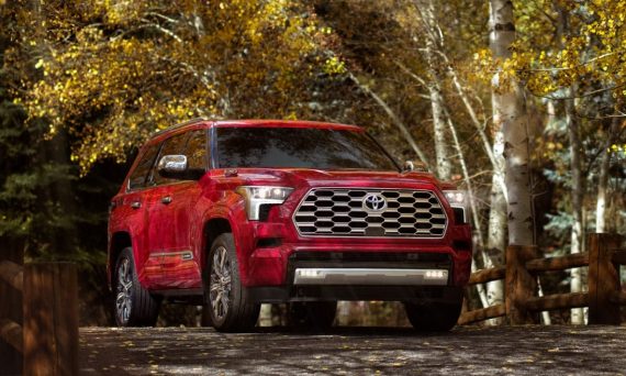 A red Toyota Sequoia driving over a bridge with golden trees in the background