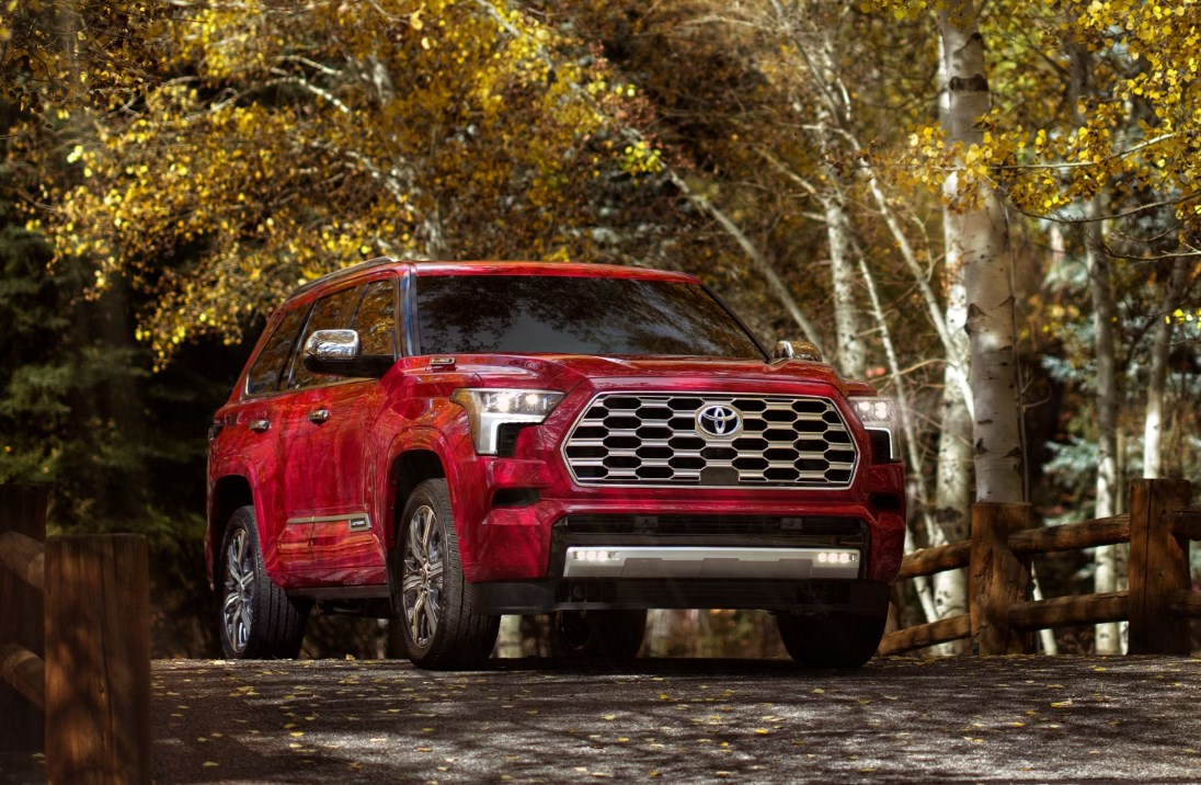 A red Toyota Sequoia driving over a bridge with golden trees in the background