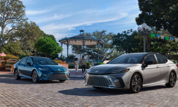 Two 2025 Toyota Camry cars parked on a sidewalk in front of a park