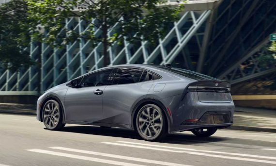 A silver 2024 Prius Prime driving down a city street in sunshine