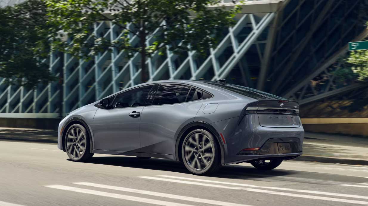 A silver 2024 Prius Prime driving down a city street in sunshine